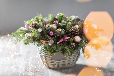 Çam kozalakları, çam dalları, eski ahşap arka plan dekoratif topları ile bir hasır sepet ile Noel ve yeni yıl tebrik kartı. Vintage tarzı seçici odak. arka plan üzerinde ışıklar çelenk