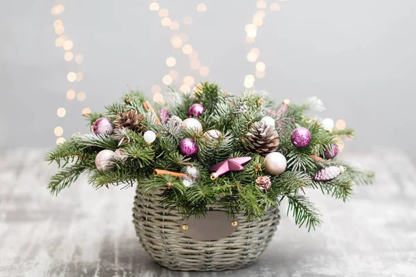 Carte de vœux de Noël ou Nouvel An avec panier en osier avec cônes de pin, branches de sapin, boules décoratives sur un vieux fond en bois. Style vintage, focus sélectif. sur les lumières de fond guirlande — Photo