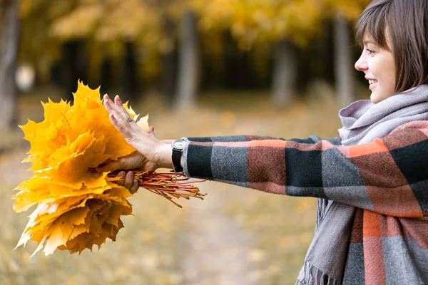 Porträt einer jungen Modefrau im Freien. brünette Frau im Herbstpark mit modischem karierten Mantel und Schal. mit gelben Blättern — Stockfoto