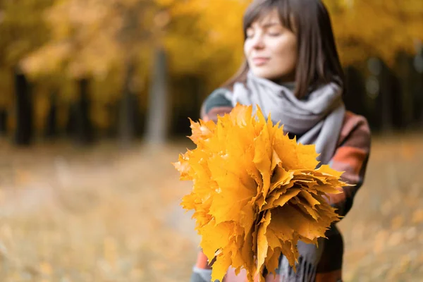 Schwerpunkt auf gelben Blättern. brünette Frau im Herbstpark mit modischem karierten Mantel und Schal. — Stockfoto