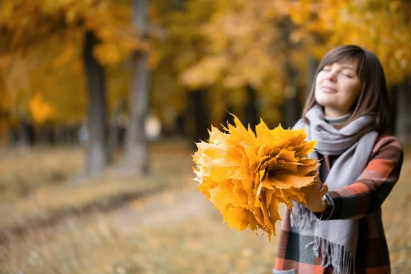 Céntrate en las hojas amarillas. Mujer morena en el parque de otoño con abrigo a cuadros de moda y bufanda . —  Fotos de Stock