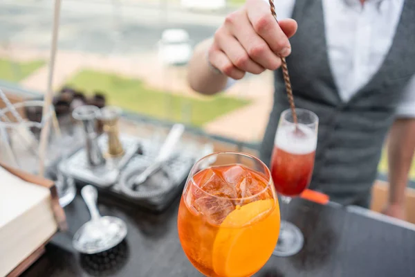 Bartender makes cocktail Aperol spritz. Misted glass, selective focus. Alcoholic beverage based on bar counter with ice cubes and oranges. outdoor party — Stock Photo, Image