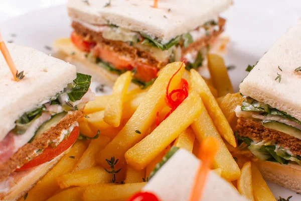 Fast food restaurant menu. Club sandwich with cheese, pIckled cucmber, tomato and smoked meat. Garnished with golden French fries potatoes