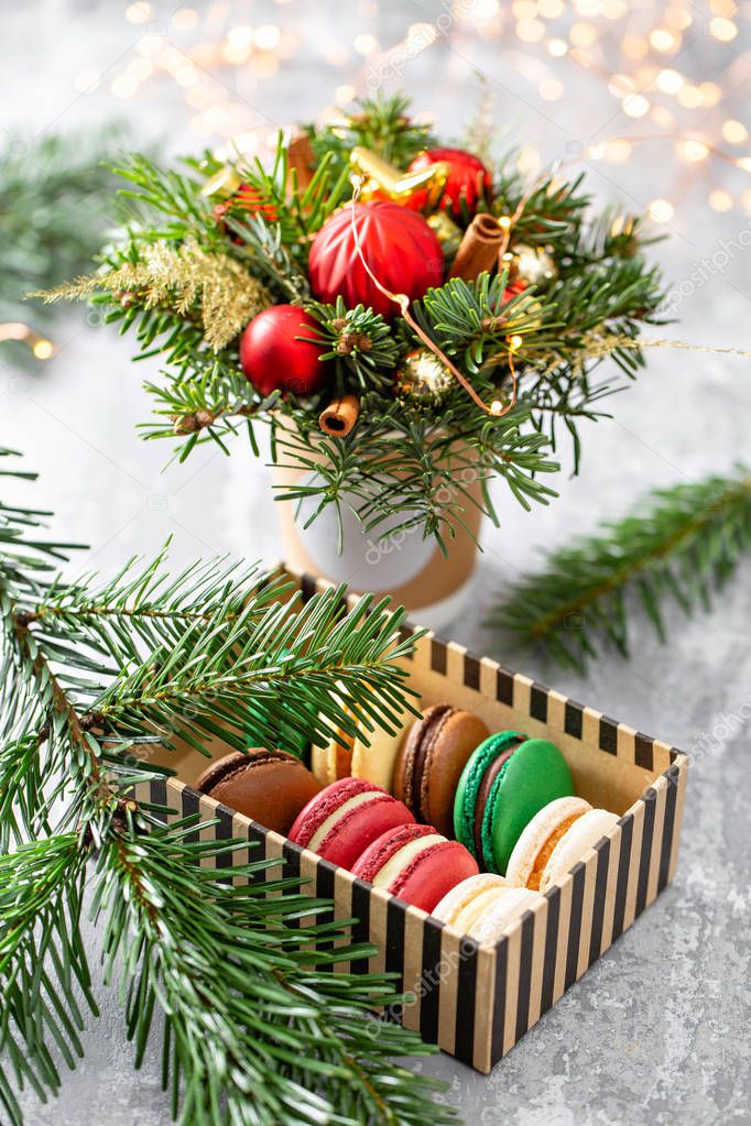 Variety of sweet macaroons in carton box. Fir branches on a gray background. Merry Christmas card. New year mood