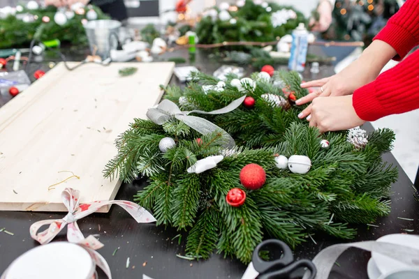 Una donna decora una corona di Natale. Mani in alto. Master class sulla realizzazione di ornamenti decorativi. Decorazione natalizia con le proprie mani. La celebrazione del nuovo anno. Negozio di fiori — Foto Stock