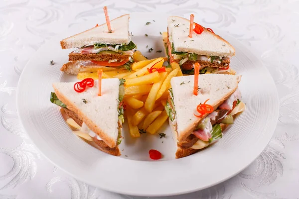 Fast food restaurant menu. Club sandwich with cheese, pIckled cucmber, tomato and smoked meat. Garnished with golden French fries potatoes