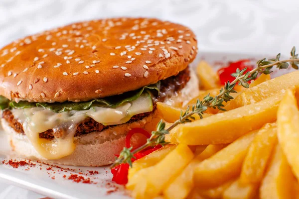 Fast food restaurant menu. Home made hamburger with the beef patties, onion, tomato, lettuce and cheese. Fresh burger close-up. Garnished with golden French fries potatoes