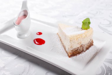 Düz New York cheesecake berry sos ile dilim bir plaka üzerinde nane yaprağı ile dekore edilmiştir. Şekerli tatlı restoranda. Sabah güneşi