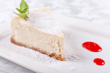 Düz New York cheesecake berry sos ile dilim bir plaka üzerinde nane yaprağı ile dekore edilmiştir. Şekerli tatlı restoranda. Sabah güneşi
