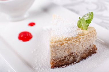 Düz New York cheesecake berry sos ile dilim bir plaka üzerinde nane yaprağı ile dekore edilmiştir. Şekerli tatlı restoranda. Sabah güneşi