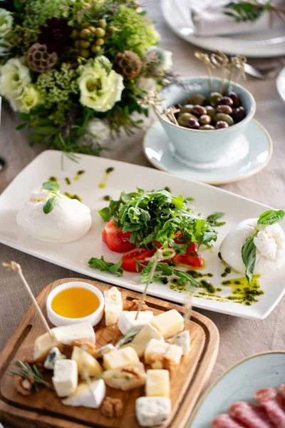 İtalyan Caprese salatası ve peynir tabağı... burrata peynir, domates ve fesleğen bitki yaprakları. Beyaz tabakta düzenlenmiş balsamik sirke