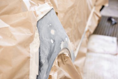 Garaj boyama servisi. Arabanın bir kısmı fünyeyle kaplanmış. Araç koruyucu kağıtlarla kaplı. Araba kaportası tamiri kazadan sonra boyamadan önce astar zımparalamayla yapılıyor..