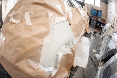 Garaj boyama servisi. Arabanın bir kısmı fünyeyle kaplanmış. Araç koruyucu kağıtlarla kaplı. Araba kaportası tamiri kazadan sonra boyamadan önce astar zımparalamayla yapılıyor..