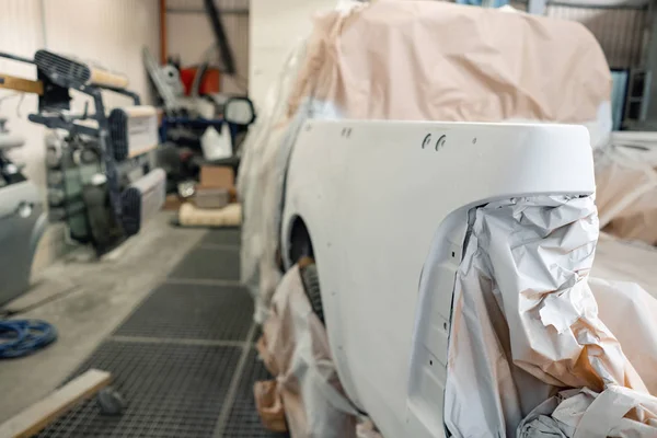 Garage painting car service. section of the car is covered with primer. vehicle is covered with protective paper. Repairing car body work after the accident by working sanding primer before painting. — Stock Photo, Image