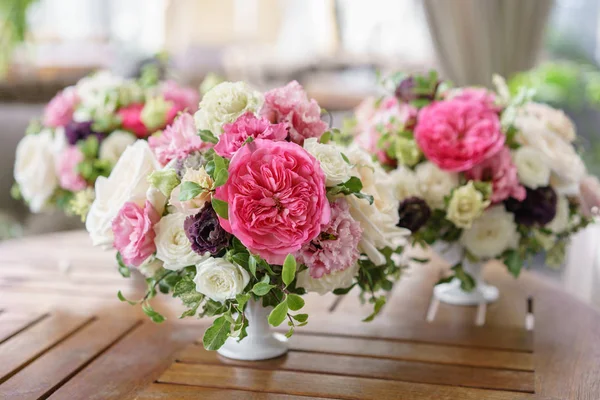 Arrangemang av färska blommor i pastellfärger. Bröllop bakgrund. bord i en restaurang. olika sorter av trädgård och buske rosor i en ljus vas på träbord — Stockfoto