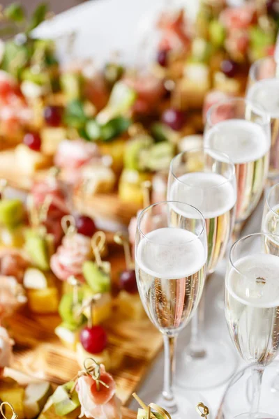 Solemne banquete feliz año nuevo. Un montón de copas de champán o vino en la mesa en el restaurante. mesa buffet con un montón de deliciosos aperitivos. canapés, bruschetta, y pequeños postres en placa de madera —  Fotos de Stock