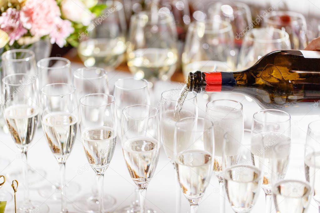 Bartender pouring champagne or wine into wine glasses on the table in restaurant. solemn wedding ceremony or happy new year banquet