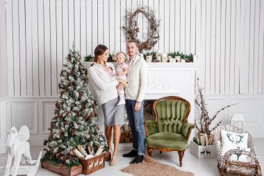 Sevgi dolu aile mutlu Noeller ve mutlu yeni yıl. Neşeli güzel insanlar. Annem ve babam küçük kızını sarılma. Anne ve bebek çocuk Noel ağacı ve beyaz şömine yakın kapalı eğleniyor.