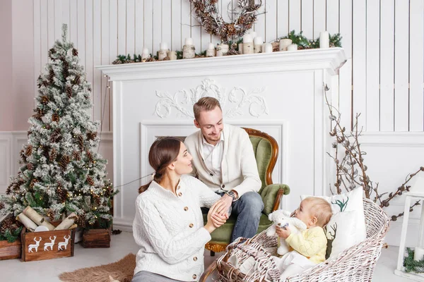 Αγαπώντας οικογένειας καλά Χριστούγεννα και Ευτυχισμένο το νέο έτος. Χαρούμενα αρκετά άτομα. Μαμά, μπαμπάς και μικρή κόρη. Γονείς και παιδί μωρό διασκεδάζουν κοντά στο χριστουγεννιάτικο δέντρο και λευκό τζάκι σε εσωτερικούς χώρους. — Φωτογραφία Αρχείου