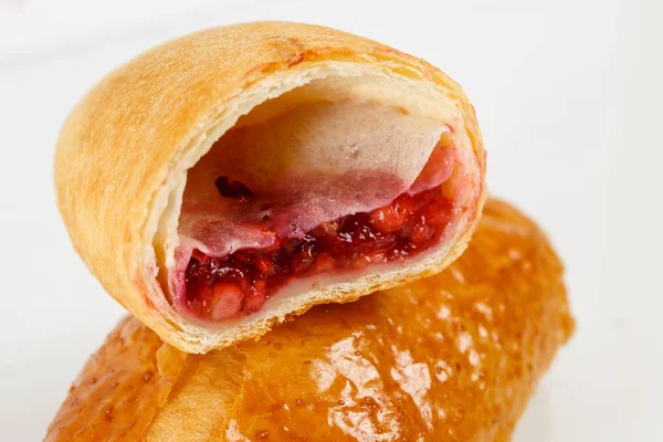 Lezzetli puf böreği tatlısı yarıya. Meyve ile lezzetli hamur işleri üzerinde açık renkli reçel. Berry, çilek veya ahududu