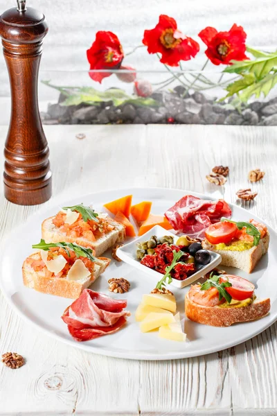 Lemez olasz előételek. Bruschetta egy koktélparadicsommal és garnélarák. Parmezán sajt, sonka, zöld kapribogyó, olívabogyó, aszalt paradicsommal, dióval. — Stock Fotó