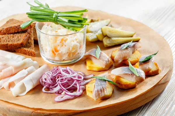 Sandwich on fried potatoes with herring, green onion. Tasty appetizer with sauerkraut, pickled cucumber, mustard on wooden Board. Rye bread and lard — Stock Image Sandwich on fried potatoes with herring, green onion. Tasty appetizer with sauerkraut, pickled cucumber, mustard on wooden Board. Rye bread and lard Stock Image