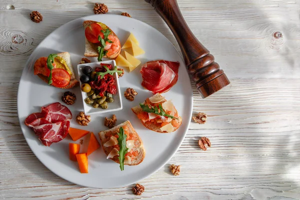 İtalyan meze plakalı. Bir kiraz domates Bruschetta ve karides. Parmesan peyniri, salam, yeşil kapari, zeytin, kurutulmuş domates ve ceviz. — Stok fotoğraf