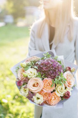Genç kız güzel bahar buket tutarak. Ortanca ve bahçe gül çiçek aranjmanı. Menekşe ve şeftali rengi çiçek. Parlak şafak veya günbatımı güneş