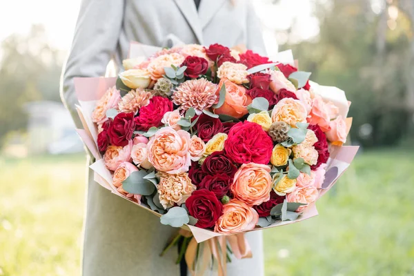 Lovely woman holding a beautiful autumn bouquet. flower arrangement with peach and red color flowers. green lawn on background. Bright dawn or sunset sun. — Stock Photo, Image