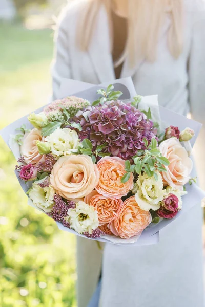 Tânăra fată deține un frumos buchet de primăvară. aranjament de flori cu hortensie și trandafiri de grădină. Violet și floare de culoare piersici. Zori strălucitori sau apus de soare — Fotografie, imagine de stoc