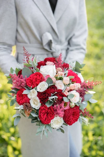 Lovely woman holding a beautiful autumn wedding bouquet. flower arrangement with white and red garden roses. Green lawn on background. Bright dawn or sunset sun — Stock Photo, Image