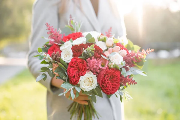 Прекрасна жінка тримає гарний осінній весільний букет. квіткова композиція з білими і червоними садовими трояндами. Зелений газон на фоні. Яскравий світанок або захід сонця — стокове фото