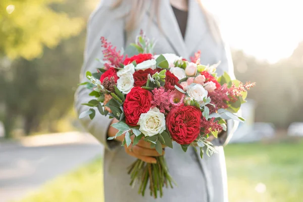 Lovely woman holding a beautiful autumn wedding bouquet. flower arrangement with white and red garden roses. Green lawn on background. Bright dawn or sunset sun — Stock Photo, Image