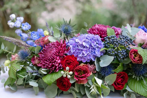 stock image Elongated floral arrangement in vintage metal vase. table setting. Blue and red color. Gorgeous bouquet of different flowers. Park on background