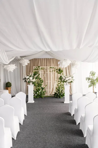 Wedding decoration, ceremony in a light tent, chairs and arch. Gorgeous bouquet of different flowers. White floral arrangement in vintage vase.