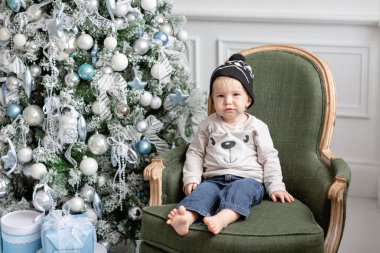Portre küçük çocuk. Yeni Yılınız Kutlu Olsun. süslü Noel ağacı. Noel sabahı parlak oturma odasında. Yeşil sandalye üzerinde duran