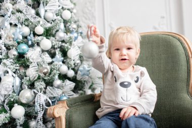 Portre küçük çocuk. Yeni Yılınız Kutlu Olsun. süslü Noel ağacı. Noel sabahı parlak oturma odasında. yeşil sandalye üzerinde oturan