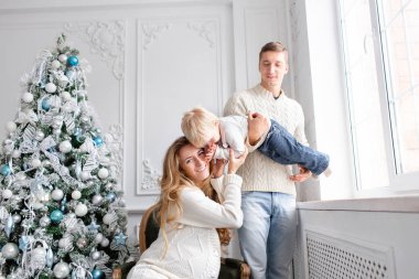 Mutlu bir aile evde eğleniyor. Noel sabahı parlak oturma odasında. Anne ile küçük oğlu. Baba, hamile anne ve bebek oğulları. Yeni Yılınız Kutlu Olsun. süslü Noel ağacı