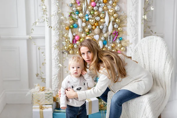 Kamera - göz şaşkınlık ile küçük oğlu genç hamile anne kucaklar. Yeni Yılınız Kutlu Olsun. süslü Noel ağacı. Noel sabahı parlak oturma odasında. — Stok fotoğraf