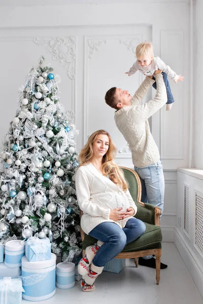 Šťastná rodina baví doma. Vánoční dopoledne v obývací pokoj. Mladí rodiče s malým synem. otec, těhotné matky a jejich chlapeček. Šťastný nový rok. zdobené vánoční strom — Stock fotografie