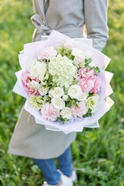 Yakın çekim güzel bahar buket elinde. pembe ve yeşil pastel renkli çiçekli narin çiçek aranjmanı. çim zemin üzerine. Parlak şafak veya günbatımı güneş.