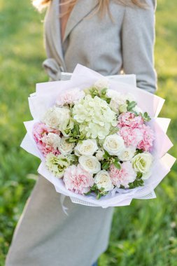 Yakın çekim güzel bahar buket elinde. pembe ve yeşil pastel renkli çiçekli narin çiçek aranjmanı. çim zemin üzerine. Parlak şafak veya günbatımı güneş.