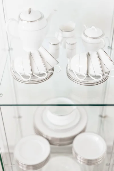 Variety of dishes in the showcase . Many rows of pure white cup. a stack of white dishes and soup bowls