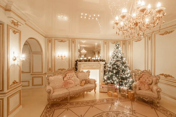 Klassisk inredning i ett vitt rum. Jul på kvällen med levande ljus. klassiska lägenheter med en vit spis, dekorerad julgran, soffa, stora fönster och ljuskrona. — Stockfoto