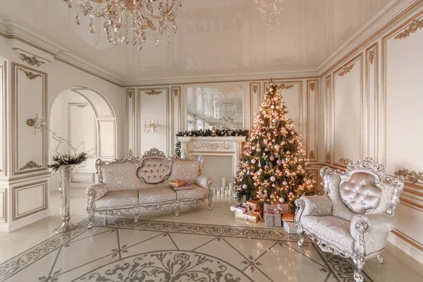 Mañana de Navidad. apartamentos de lujo clásicos con chimenea blanca, árbol de Navidad decorado, sofá, grandes ventanales y lámpara de araña . — Foto de Stock