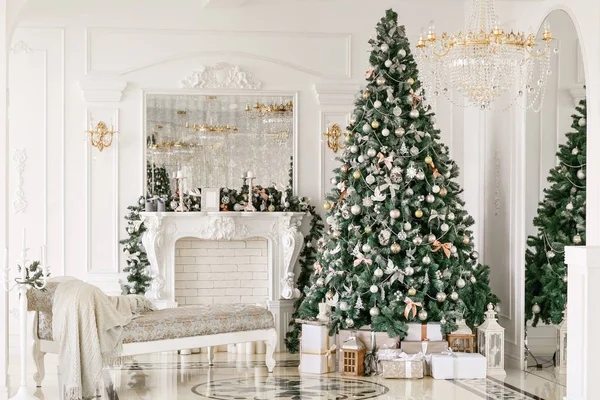 Regalos en el árbol de Navidad. Mañana de Navidad. apartamentos de lujo clásicos con chimenea blanca, sofá, ventanas grandes y lámpara de araña . — Foto de Stock