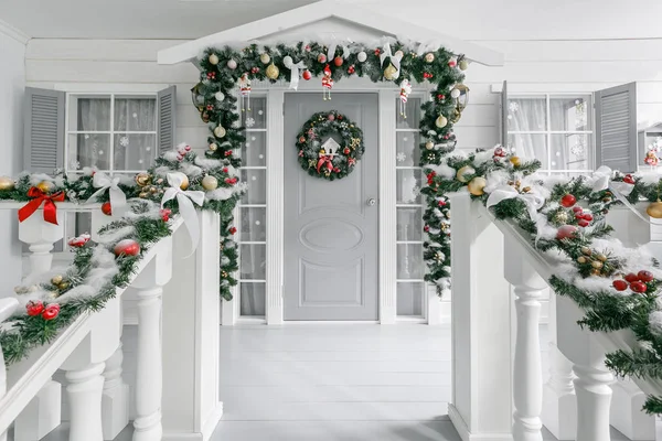 クリスマスの朝。休日の家の入口が飾られています。クリスマス装飾。モミの木の枝や手すりのライトのガーランド — ストック写真