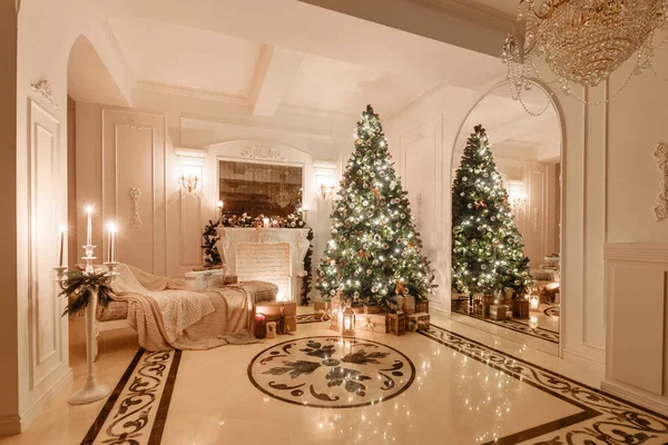 Interior clássico de um quarto branco. Noite de Natal à luz das velas. apartamentos clássicos com uma lareira branca, árvore de natal decorada, sofá, janelas grandes e lustre . — Fotografia de Stock