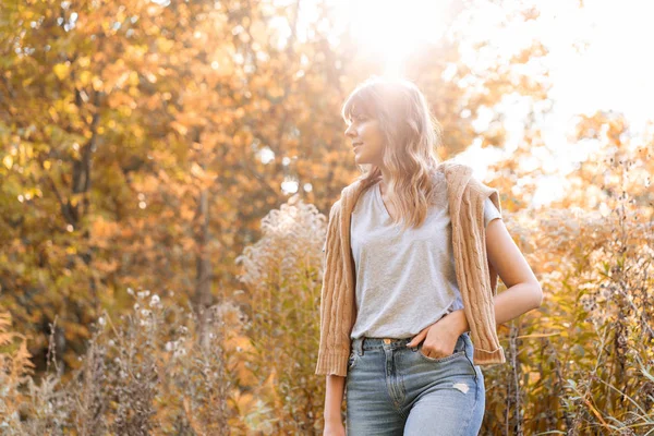 Retrato de mujer joven en el parque de otoño. Árboles con follaje amarillo en el fondo, hermosa luz del atardecer. Jersey caliente en los hombros —  Fotos de Stock