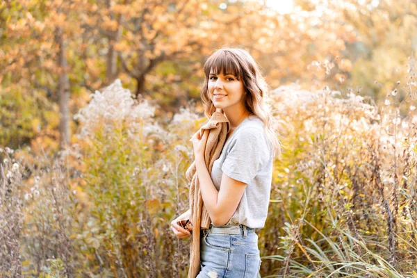 Porträt einer jungen Frau im Herbstpark. Bäume mit gelbem Laub im Hintergrund, schönes Sonnenuntergangslicht. warmer Pullover auf den Schultern — Stockfoto